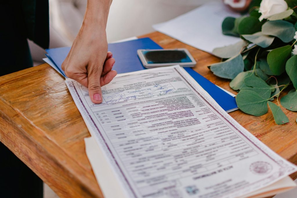 Person pointing at a marriage certificate on a wooden table.